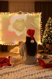Photo of MYKOLAIV, UKRAINE - DECEMBER 24, 2020: Woman watching The Grinch movie via video projector in room. Cozy winter holidays atmosphere