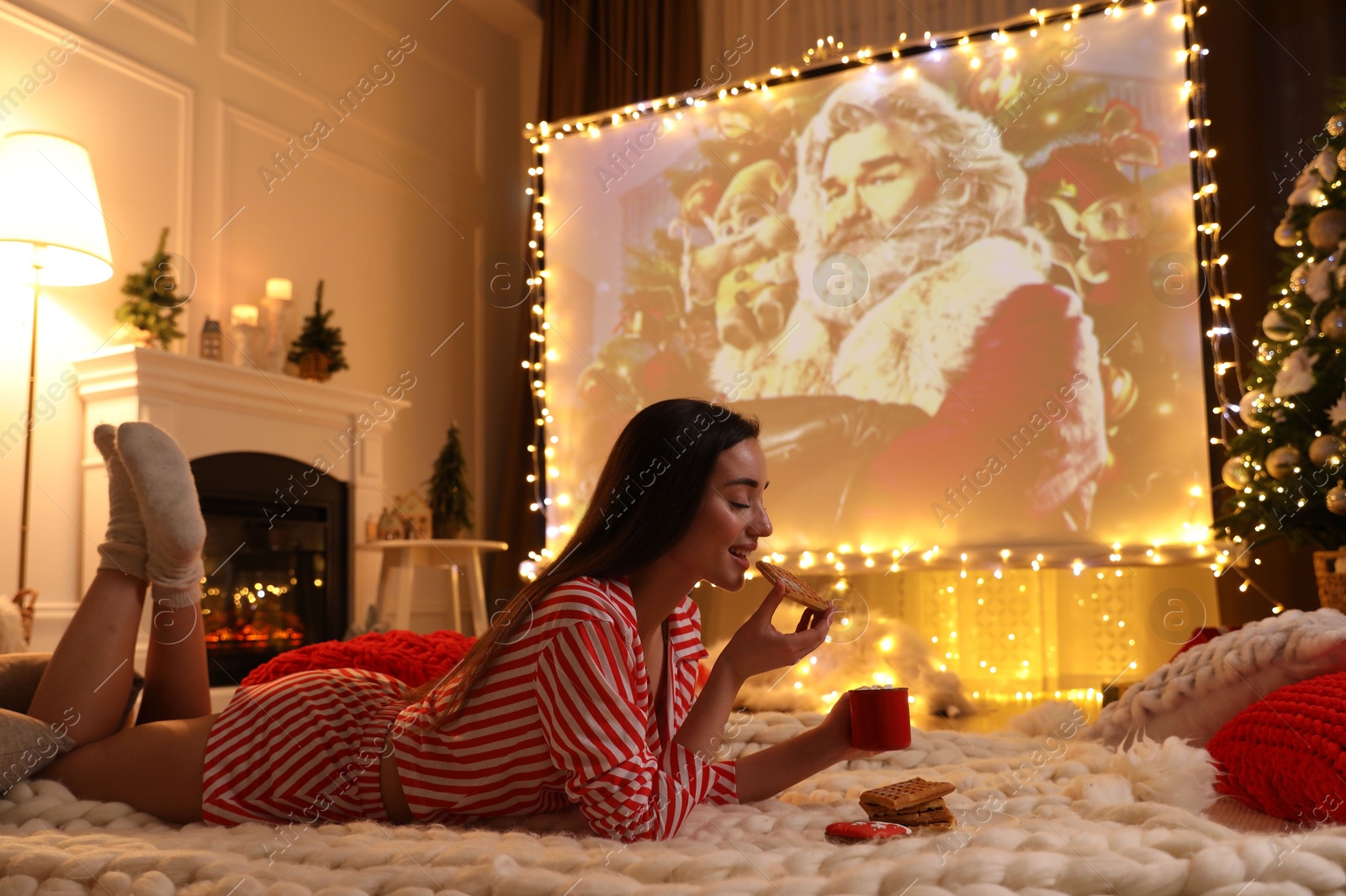 MYKOLAIV, UKRAINE - DECEMBER 24, 2020: Woman watching The Christmas Chronicles movie via video projector in room. Cozy winter holidays atmosphere Photo of MYKOLAIV, UKRAINE - DECEMBER 24, 2020: Woman watching The Christmas Chronicles movie via video projector in room. Cozy winter holidays atmosphere