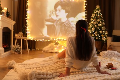 Photo of MYKOLAIV, UKRAINE - DECEMBER 24, 2020: Woman watching Harry Potter and Philosopher's Stone movie via video projector in room. Cozy winter holidays atmosphere