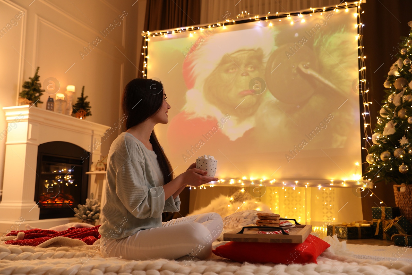 MYKOLAIV, UKRAINE - DECEMBER 24, 2020: Woman watching The Grinch movie via video projector in room. Cozy winter holidays atmosphere Photo of MYKOLAIV, UKRAINE - DECEMBER 24, 2020: Woman watching The Grinch movie via video projector in room. Cozy winter holidays atmosphere
