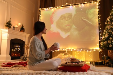 Photo of MYKOLAIV, UKRAINE - DECEMBER 24, 2020: Woman watching The Grinch movie via video projector in room. Cozy winter holidays atmosphere