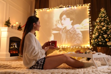 Photo of MYKOLAIV, UKRAINE - DECEMBER 24, 2020: Woman watching Harry Potter and Philosopher's Stone movie via video projector in room. Cozy winter holidays atmosphere