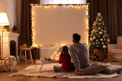 Photo of Father and daughter watching movie using video projector at home. Cozy Christmas atmosphere