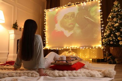 Photo of MYKOLAIV, UKRAINE - DECEMBER 24, 2020: Woman watching The Grinch movie via video projector in room. Cozy winter holidays atmosphere