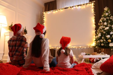 Photo of Family watching movie using video projector at home. Cozy Christmas atmosphere