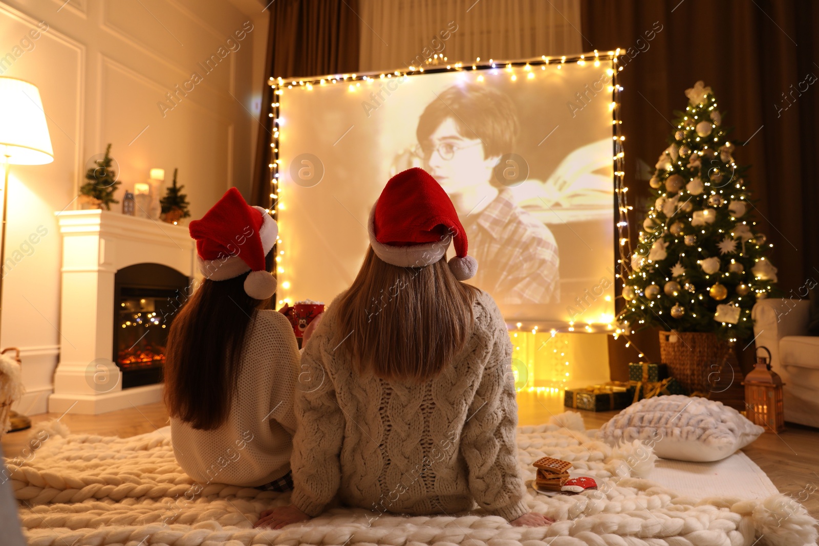 MYKOLAIV, UKRAINE - DECEMBER 24, 2020: Women watching Harry Potter and Philosopher's Stone movie via video projector in room. Cozy winter holidays atmosphere Photo of MYKOLAIV, UKRAINE - DECEMBER 24, 2020: Women watching Harry Potter and Philosopher's Stone movie via video projector in room. Cozy winter holidays atmosphere