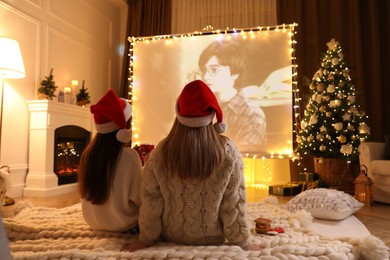 Photo of MYKOLAIV, UKRAINE - DECEMBER 24, 2020: Women watching Harry Potter and Philosopher's Stone movie via video projector in room. Cozy winter holidays atmosphere