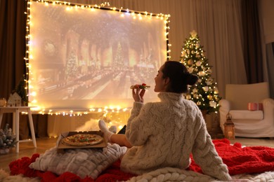 Photo of MYKOLAIV, UKRAINE - DECEMBER 24, 2020: Woman watching Harry Potter and Philosopher's Stone movie via video projector in room. Cozy winter holidays atmosphere