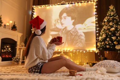 Photo of MYKOLAIV, UKRAINE - DECEMBER 24, 2020: Woman watching Harry Potter and Philosopher's Stone movie via video projector in room. Cozy winter holidays atmosphere