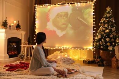 Photo of MYKOLAIV, UKRAINE - DECEMBER 24, 2020: Woman watching The Grinch movie via video projector in room. Cozy winter holidays atmosphere