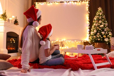Photo of Mother and daughter watching movie using video projector at home. Cozy Christmas atmosphere