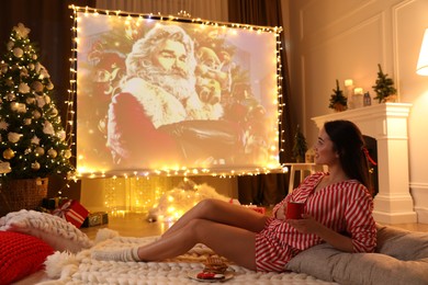 Photo of MYKOLAIV, UKRAINE - DECEMBER 24, 2020: Woman watching The Christmas Chronicles movie via video projector in room. Cozy winter holidays atmosphere