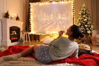Photo of MYKOLAIV, UKRAINE - DECEMBER 24, 2020: Woman watching Harry Potter and Philosopher's Stone movie via video projector in room. Cozy winter holidays atmosphere