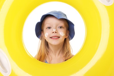 Photo of Smiling little girl with sun protection cream on her face looking through hole of inflatable ring against white background