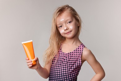 Photo of Cute little girl with tube of sun protection product on grey background