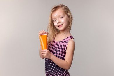 Photo of Smiling little girl with tube of sun protection product on grey background