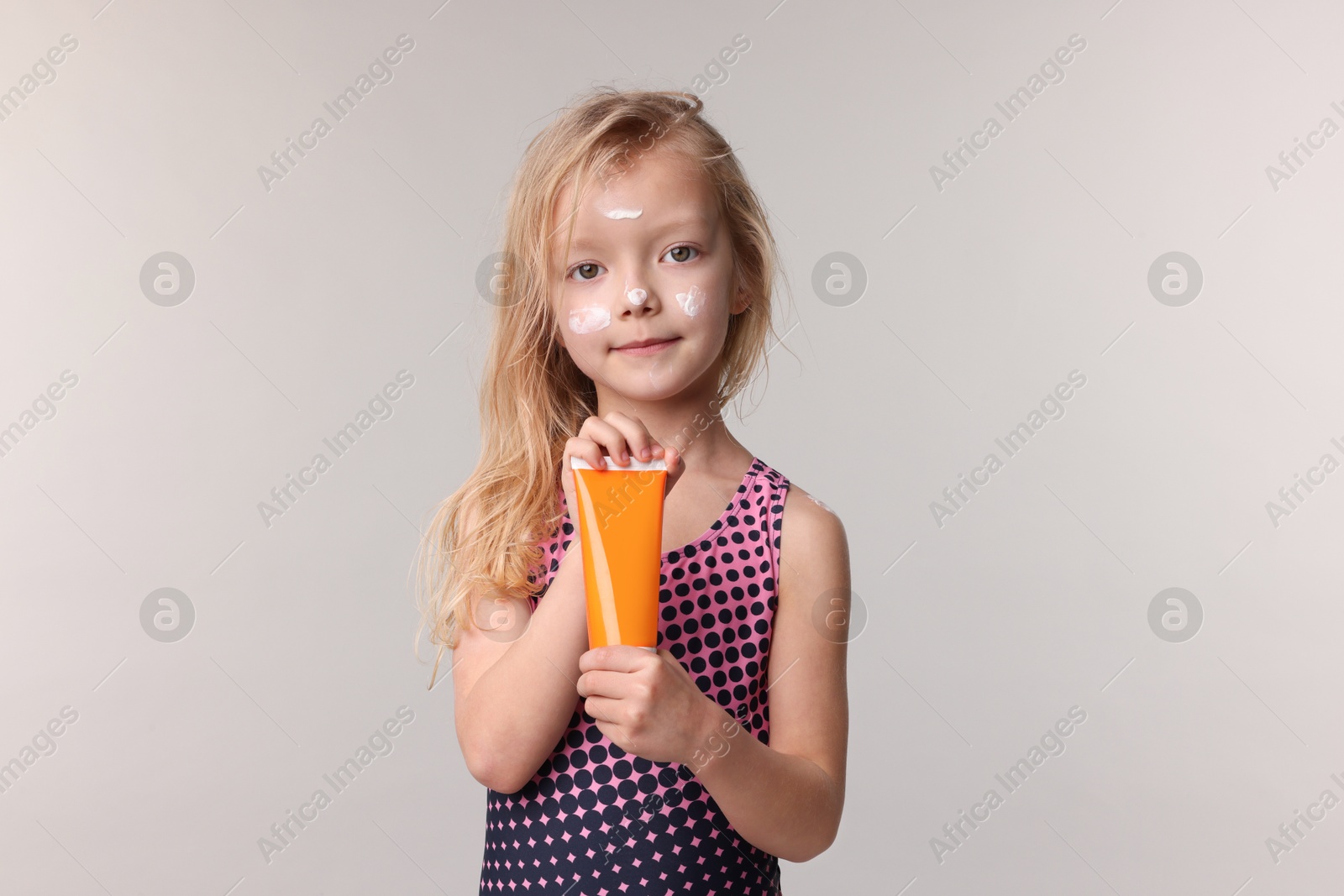 Photo of Cute little girl with tube of sun protection product on grey background