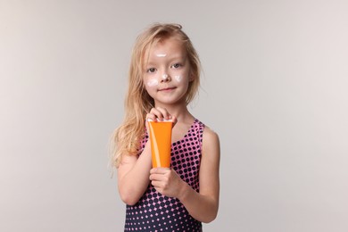 Photo of Cute little girl with tube of sun protection product on grey background