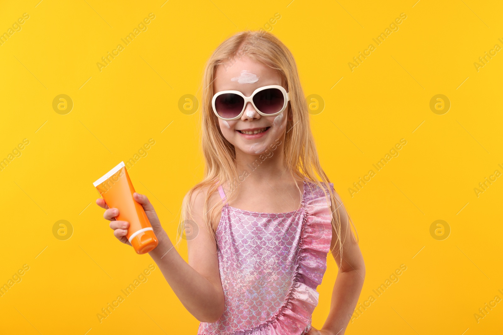 Smiling little girl with tube of sun protection cream against yellow background Photo of Smiling little girl with tube of sun protection cream against yellow background