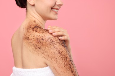 Photo of Smiling woman applying body scrub onto her shoulder against pink background, closeup. Space for text