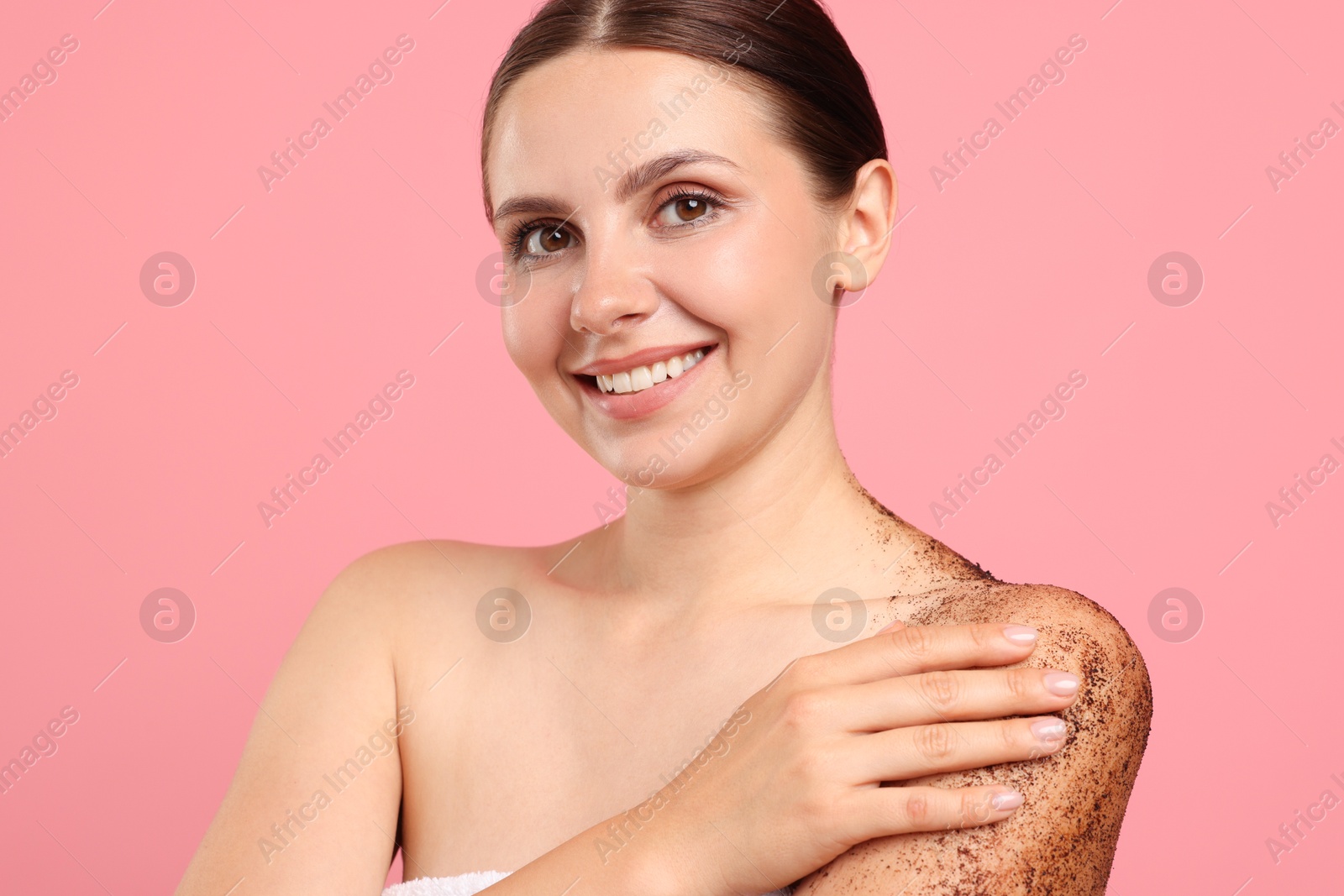 Smiling woman applying body scrub onto her shoulder against pink background Photo of Smiling woman applying body scrub onto her shoulder against pink background