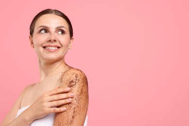 Photo of Smiling woman applying body scrub onto her arm against pink background. Space for text