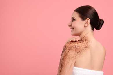 Photo of Smiling woman applying body scrub onto her shoulder against pink background. Space for text