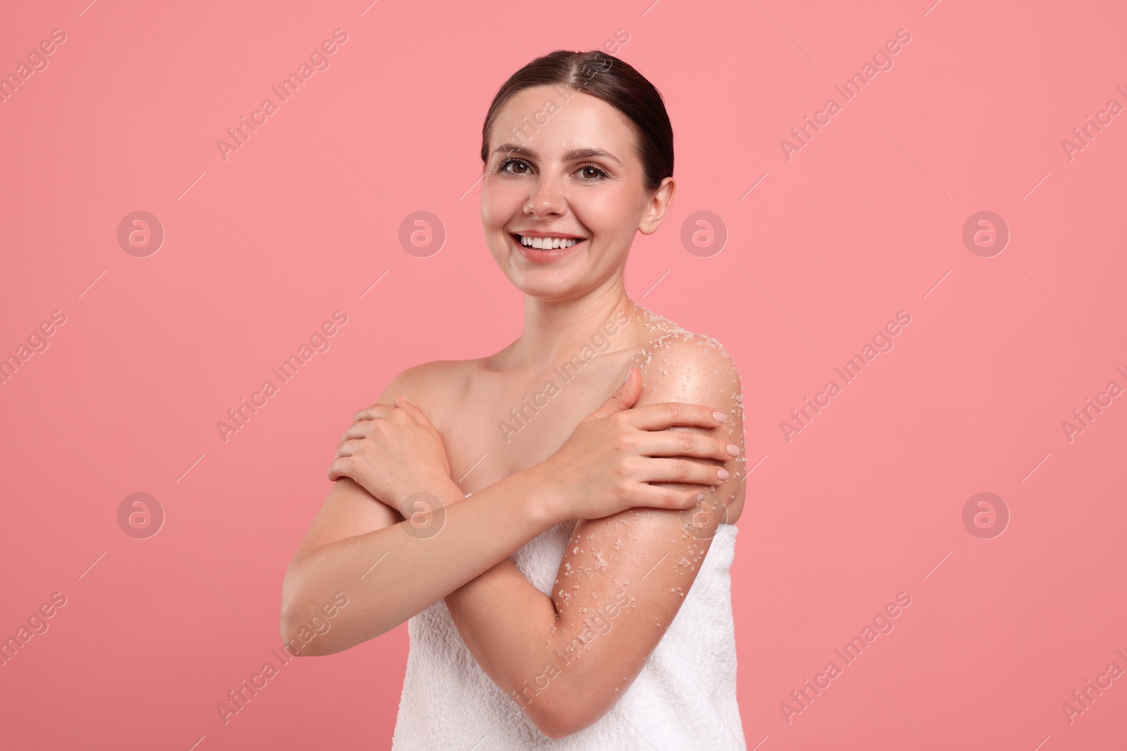 Smiling woman applying body scrub onto her arm against pink background Photo of Smiling woman applying body scrub onto her arm against pink background