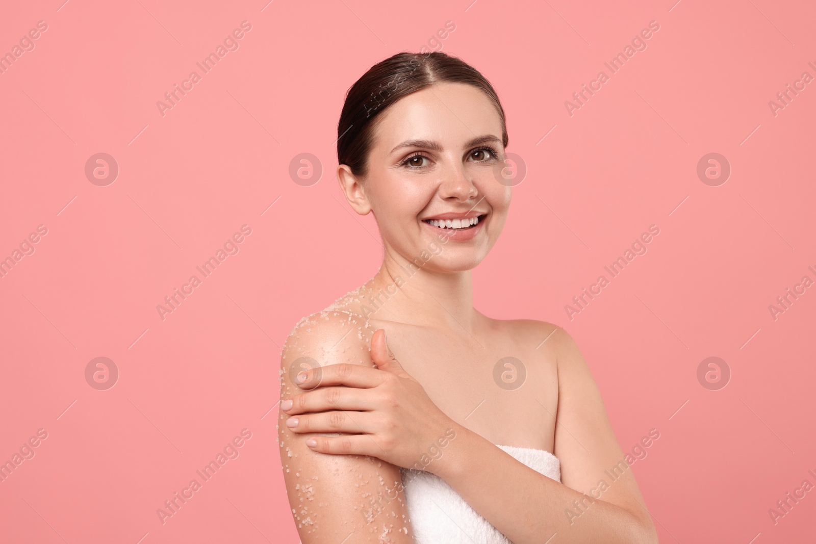 Smiling woman applying body scrub onto her arm against pink background Photo of Smiling woman applying body scrub onto her arm against pink background