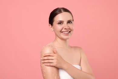 Photo of Smiling woman applying body scrub onto her arm against pink background