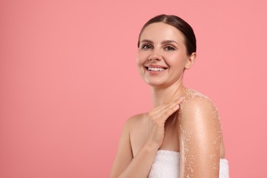 Photo of Smiling woman applying body scrub onto her shoulder against pink background. Space for text