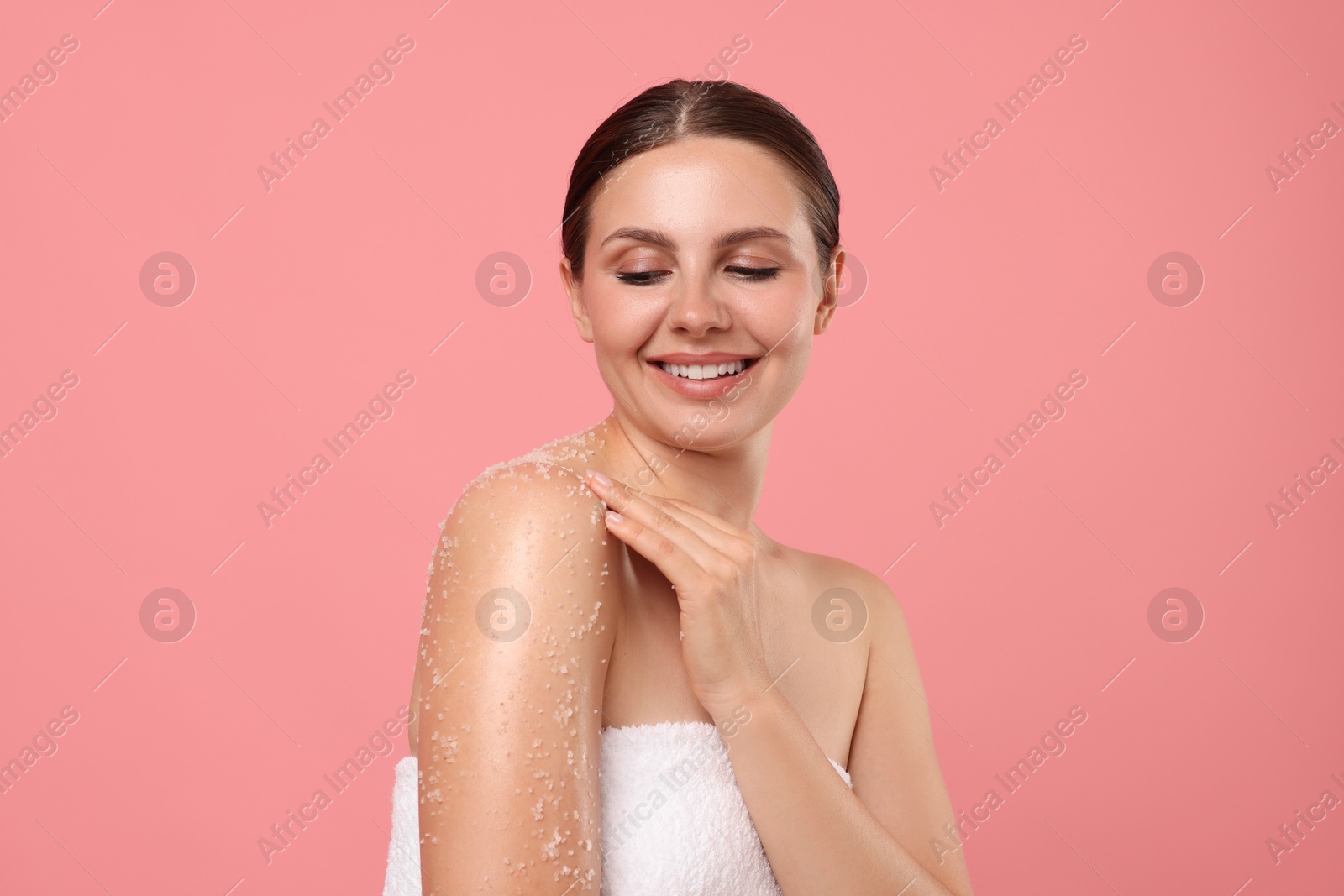 Smiling woman applying body scrub onto her shoulder against pink background Photo of Smiling woman applying body scrub onto her shoulder against pink background