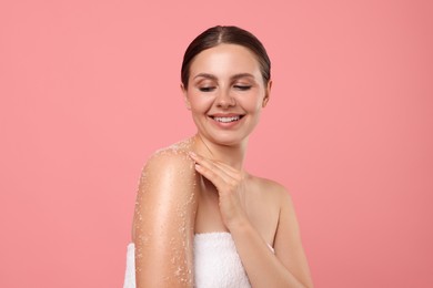 Photo of Smiling woman applying body scrub onto her shoulder against pink background