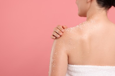 Photo of Woman applying body scrub onto her shoulder against pink background, back view. Space for text