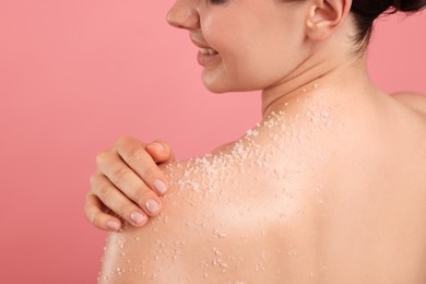 Photo of Smiling woman applying body scrub onto her shoulder against pink background