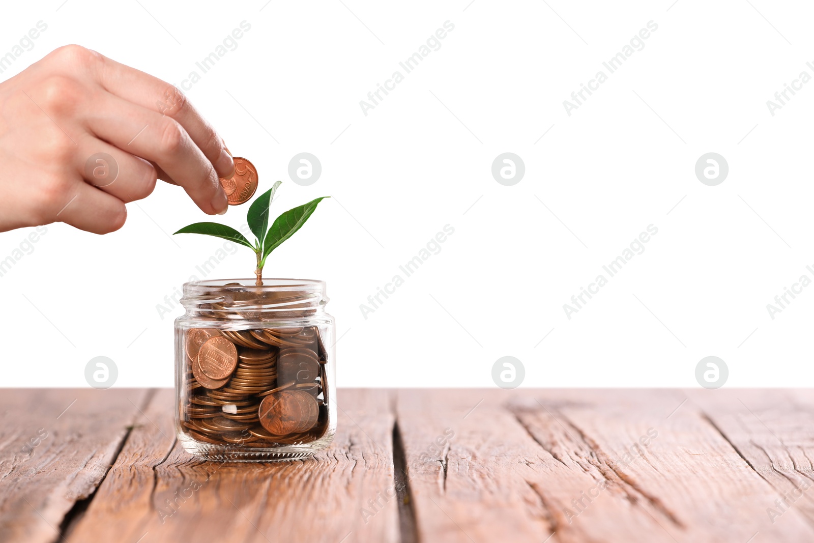Investment concept. Woman putting coin into glass jar at wooden table against light background, closeup. Space for text Photo of Investment concept. Woman putting coin into glass jar at wooden table against light background, closeup. Space for text