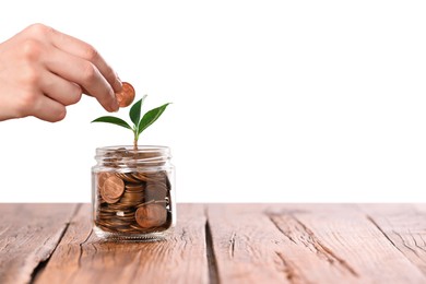 Photo of Investment concept. Woman putting coin into glass jar at wooden table against light background, closeup. Space for text