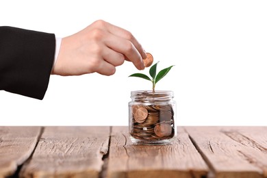 Photo of Investment concept. Woman putting coin into glass jar at wooden table against light background, closeup
