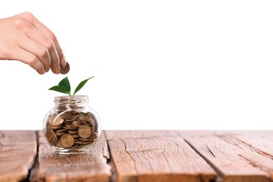 Photo of Investment concept. Woman putting coin into glass jar at wooden table against light background, closeup. Space for text