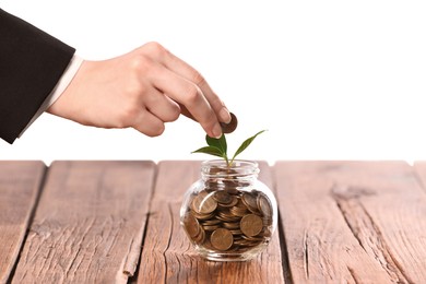 Photo of Investment concept. Woman putting coin into glass jar at wooden table against light background, closeup
