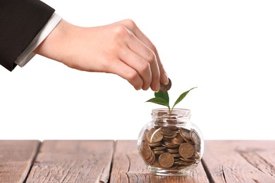 Photo of Investment concept. Woman putting coin into glass jar at wooden table against light background, closeup