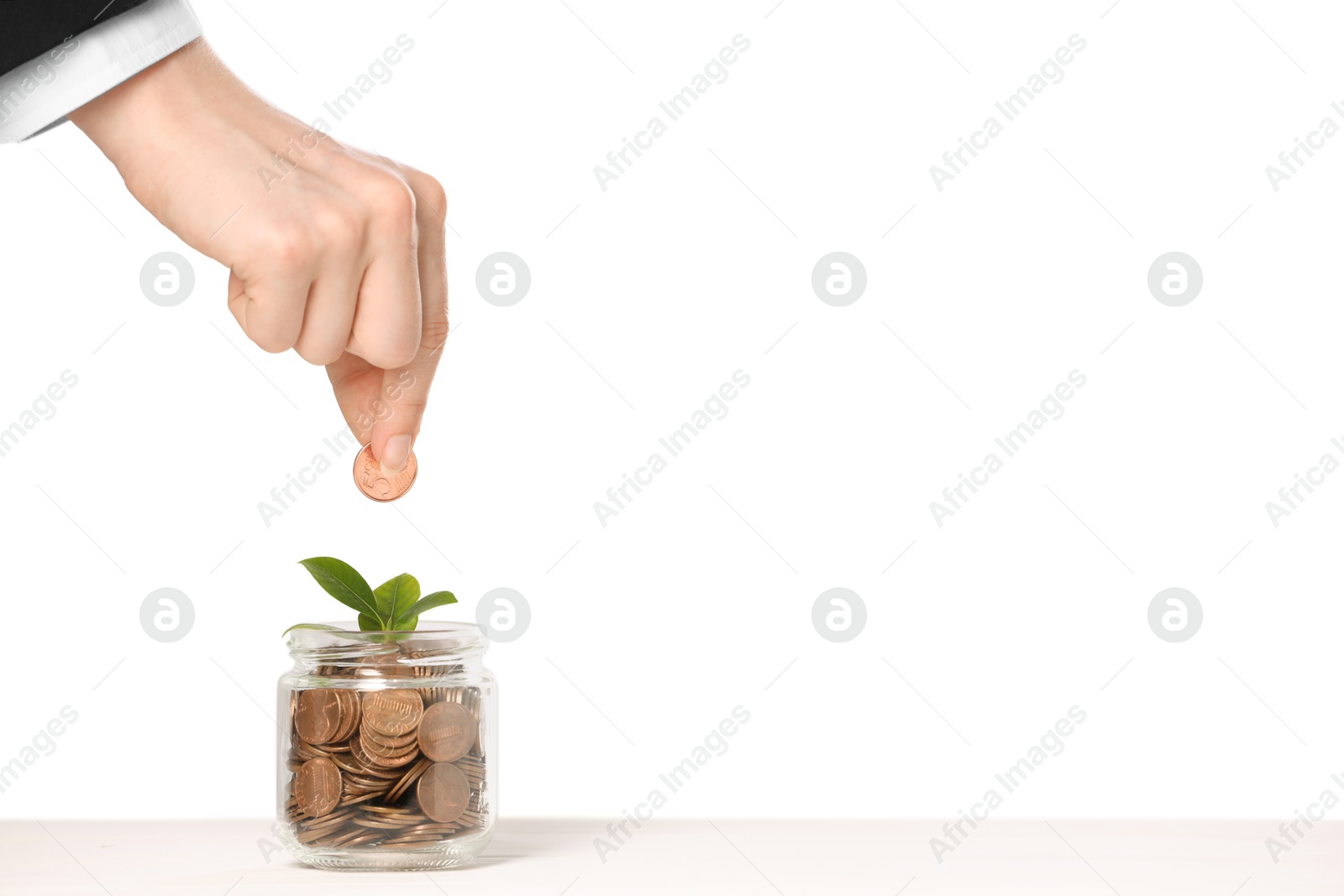 Investment concept. Woman putting coin into glass jar at white table against light background, closeup. Space for text Photo of Investment concept. Woman putting coin into glass jar at white table against light background, closeup. Space for text