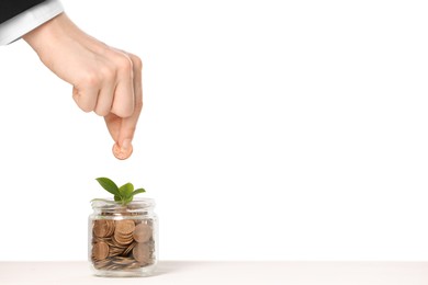 Photo of Investment concept. Woman putting coin into glass jar at white table against light background, closeup. Space for text