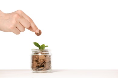 Photo of Investment concept. Woman putting coin into glass jar at white table against light background, closeup. Space for text