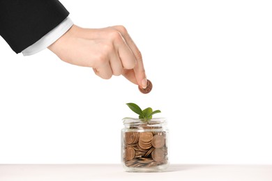Photo of Investment concept. Woman putting coin into glass jar at white table against light background, closeup