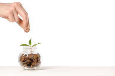 Photo of Investment concept. Woman putting coin into glass jar at white table against light background, closeup. Space for text