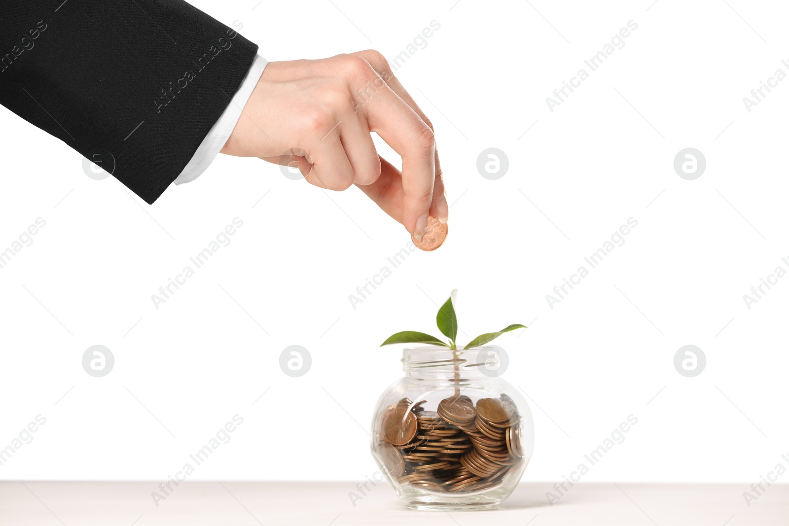 Investment concept. Woman putting coin into glass jar at white table against light background, closeup Photo of Investment concept. Woman putting coin into glass jar at white table against light background, closeup