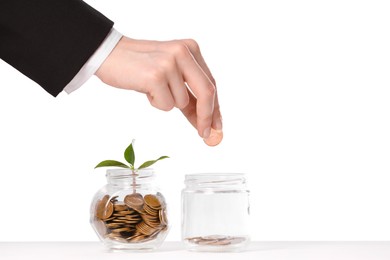 Photo of Investment concept. Woman putting coin into glass jar at white table against light background, closeup. Space for text