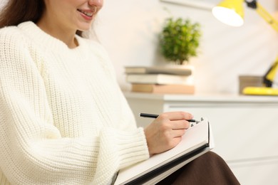Photo of Woman writing in planner at home, closeup. Space for text