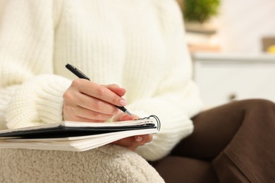 Photo of Woman writing in planner on armchair indoors, closeup